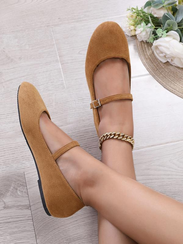 Brown suede shoes with gold chain strap on a light wooden floor.