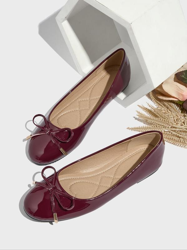 Pair of burgundy patent leather flats with bow details on a white background