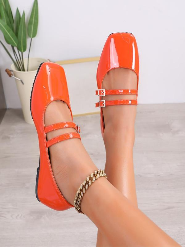 Orange flat shoes with thin straps worn by a person on a light wooden floor.
