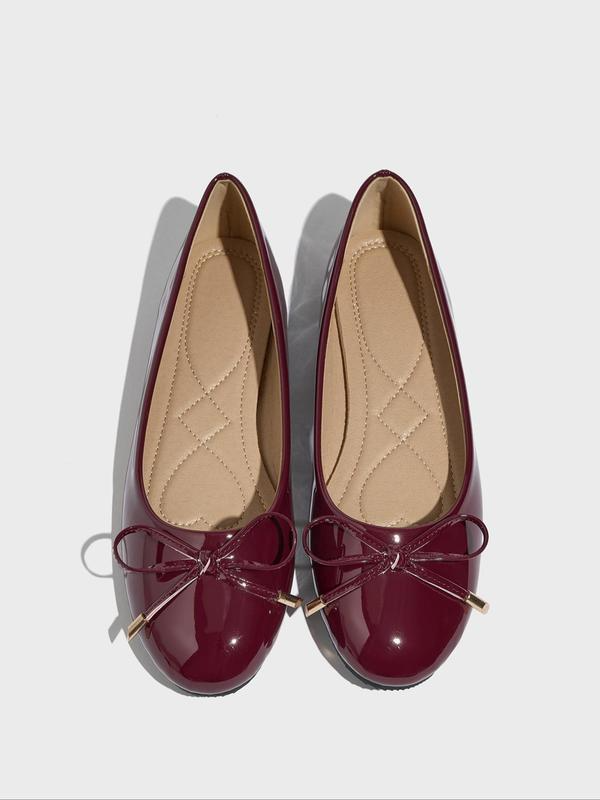 Pair of maroon ballet flats with a bow on a light gray background