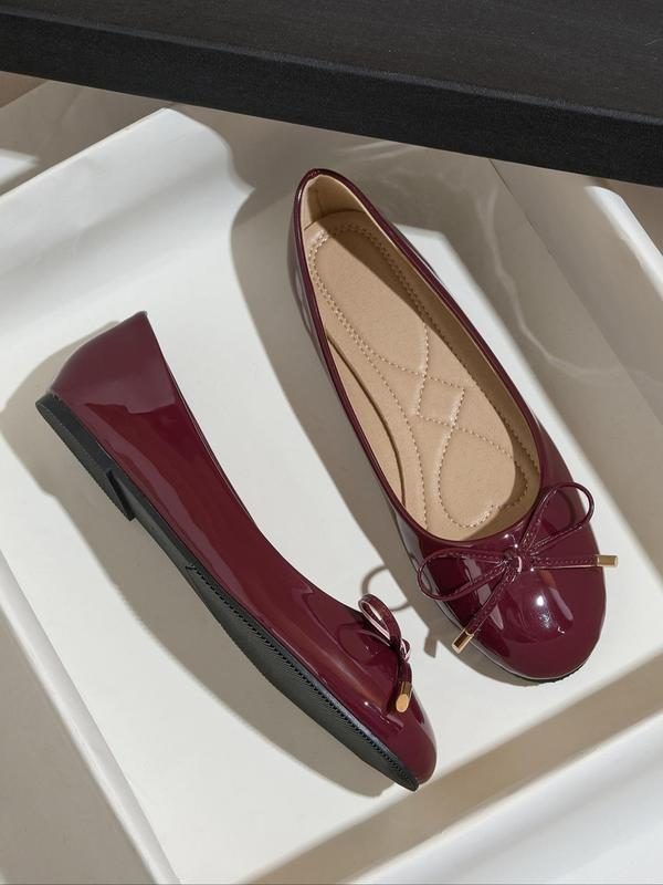 Pair of maroon patent leather shoes with a bow on a white surface.