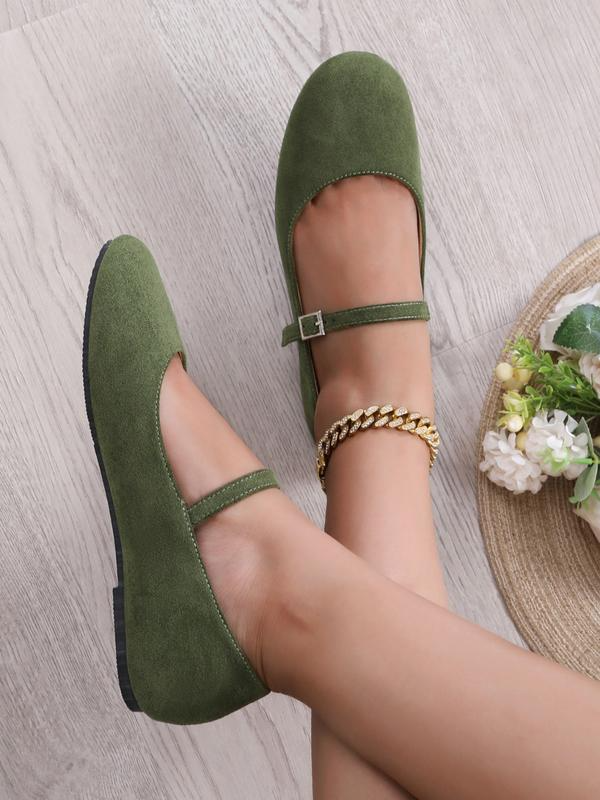 Green suede shoes worn by a person on a light wooden floor.