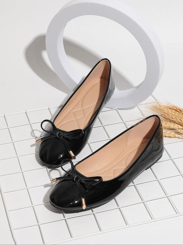 Black patent leather shoes with bow details on a white tiled background
