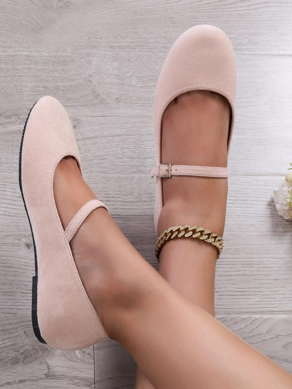 Beige flat shoes worn on a light wooden floor with a gold bracelet.