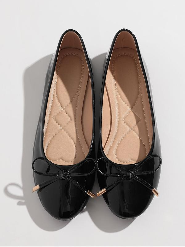Black patent leather flats with bow detail on a light gray background
