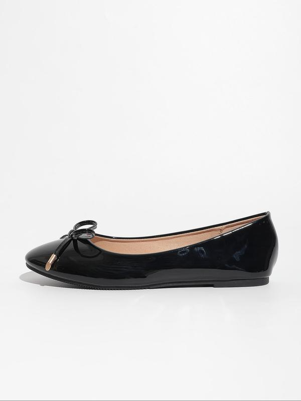 Black patent leather flat shoe with a bow on a white background