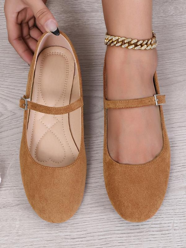 Brown flat shoes being worn on a light wooden floor.