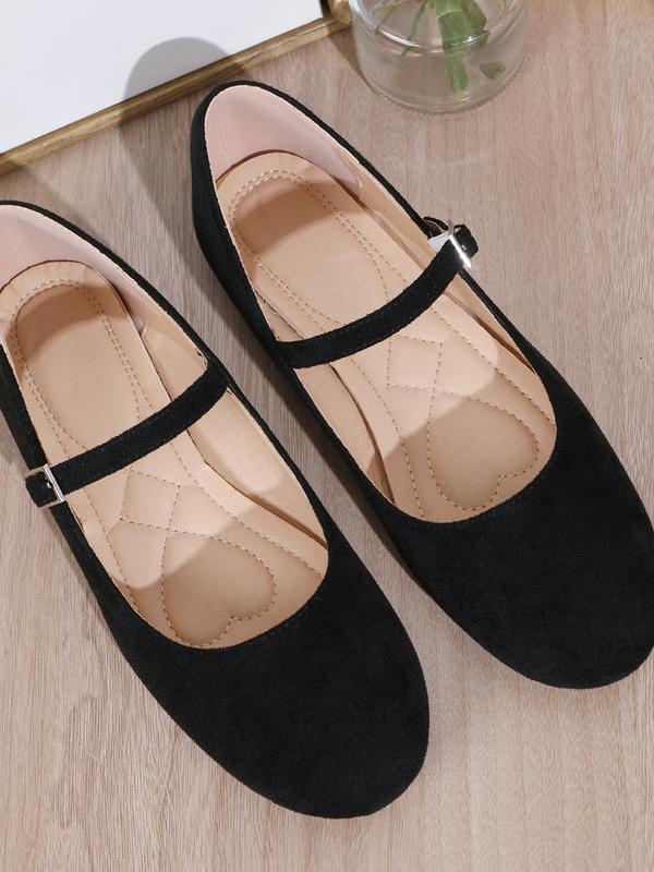 Black flat shoes with a strap on a light wooden surface