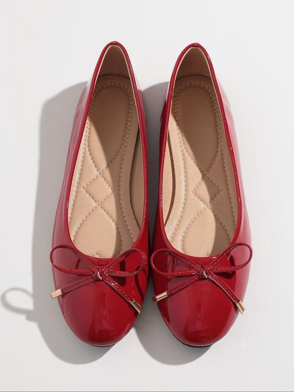Red patent leather shoes with bow details on a white background